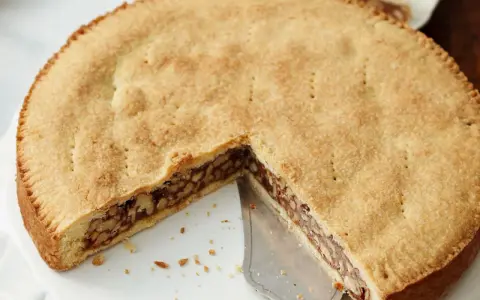 Eine köstliche Engadiner Nusstorte mit goldbraunem Teig und einer reichhaltigen Nussfüllung, gerade angeschnitten.