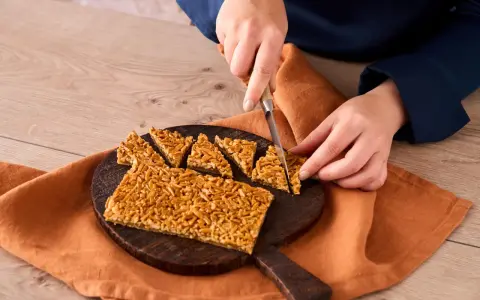 Ein Nussecken Rezept wird hier gezeigt. Eine Person schneidet die süßen Nussecken auf einem Holzbrett.