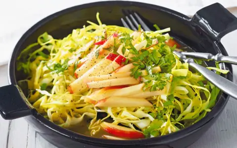 Frischer Spitzkohl Salat mit Apfelspalten und Kräutern, appetitlich in einer schwarzen Schüssel serviert.