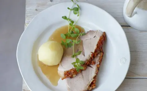 Ein knuspriger Schweinebraten mit Soße und Klößen, perfekt für ein deftiges Schweinebraten Rezept. Frisch garniert mit Kräutern.