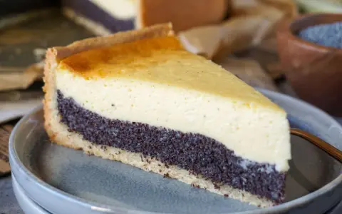 Ein Stück Mohnkuchen mit cremigem Käse-Topping und Mohnback-Schicht auf einem grauen Teller.