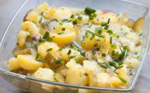 Ein köstlicher Kartoffelsalat ohne Mayo, mit Gurkenstücken und frischem Schnittlauch garniert, in einer Glasschüssel.