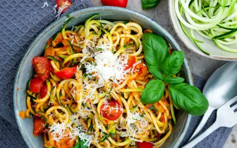 Herzhafte Zucchini-Nudeln mit Tomaten und Basilikum, bestreut mit Parmesan. Ein leichter Genuss!