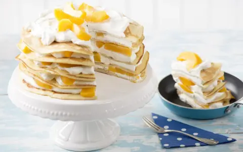 Eine köstliche Pfannkuchen Torte mit Pfirsichen und Sahne, auf einem weißen Tortenständer und ein Stück in einer kleinen Pfanne.