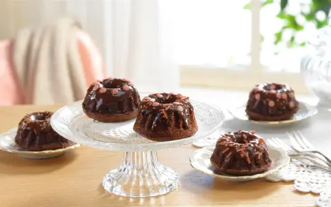 Schokoladen-Mini-Gugelhupf dekorieren mit Schokoglasur und bunten Streuseln auf einem Tortenständer.