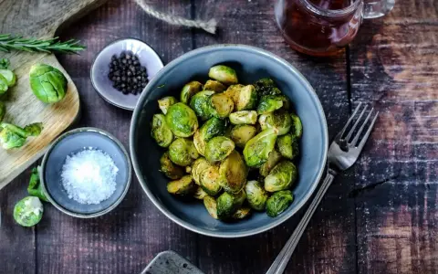 Gerösteter Rosenkohl in einer Schüssel, bereit für leckere Rezepte mit Rosenkohl. Daneben Salz, Pfeffer und ein Glas Sirup.