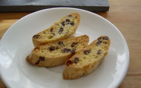 Drei knusprige Cantuccini mit Schokolade liegen auf einem weißen Teller.