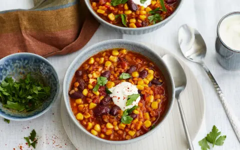 Herzhaftes Chili sin Carne mit Mais, Bohnen und Linsen, garniert mit einem Klecks Sauerrahm und frischer Petersilie.