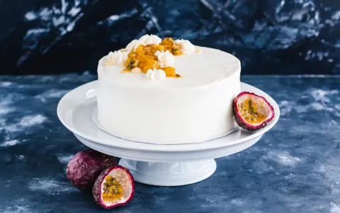 Eine weiße Maracuja Torte mit frischer Maracuja-Frucht und Sahnetupfern, umgeben von ganzen und halbierten Maracujas.