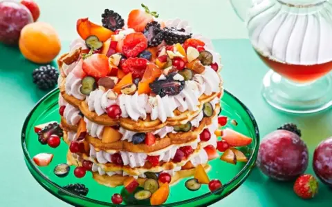 Eine mehrstöckige Waffeltorte mit Mascarpone-Creme, Beeren, Pfirsichen und Nüssen, garniert mit frischen Früchten.