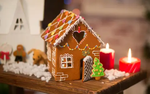 Ein zauberhaftes Lebkuchenhaus, das Lust macht, es selber zu machen. Verziert mit bunten Smarties und Zuckerguss, steht es neben Kerzen und Weihnachtsfiguren.