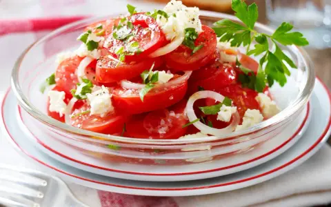 Frischer Tomaten Feta Salat mit Zwiebelringen und Petersilie, garniert mit schwarzem Pfeffer und Meersalz.