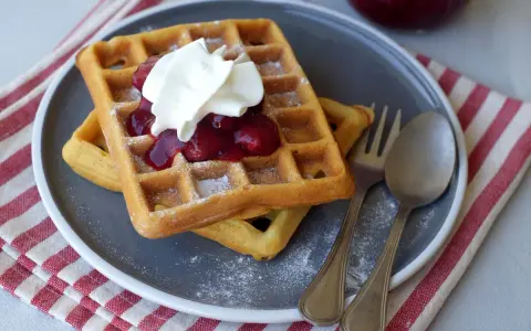 Zwei Hefewaffeln mit Trockenhefe, garniert mit Kirschkompott und Sahne, bestäubt mit Puderzucker.
