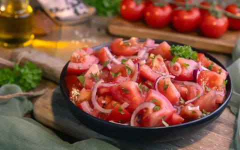 Frischer Tomatensalat mit roten Zwiebeln und Petersilie, serviert in einer schwarzen Schüssel. Das Tomatensalat Dressing ist leicht und würzig.