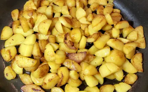 Goldbraune bratkartoffeln aus gekochten kartoffeln brutzeln in der Pfanne. Sie sind knusprig und duften herrlich.