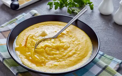 Cremige Polenta mit Butter, ein einfaches und köstliches polenta rezept, serviert in einer schwarzen Schüssel auf kariertem Tuch.