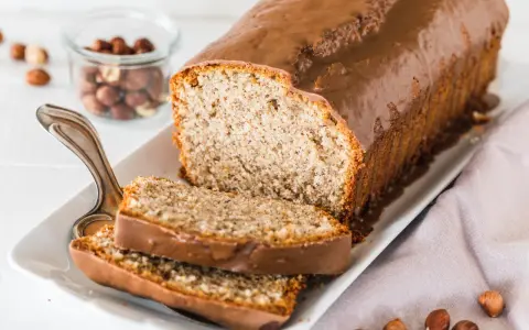 Saftiger Mohn Nuss Kuchen mit Schokoladenglasur, daneben ein Glas mit Haselnüssen und zwei angeschnittene Scheiben.