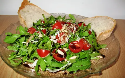 Frischer Rucola Salat mit Kirschtomaten, Pinienkernen und Parmesan, beträufelt mit Balsamico-Dressing. Dazu knuspriges Brot.