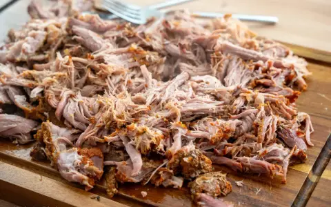 Ein Haufen zartes, **gezupftes Fleisch** liegt auf einem Holzbrett, bereit für leckere Sandwiches oder Tacos. Eine Gabel liegt daneben.