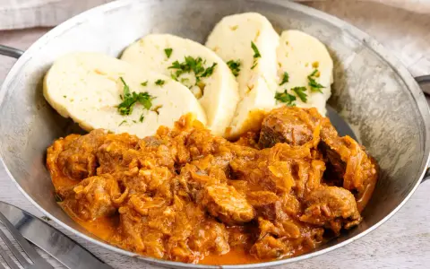 Herzhaftes Szegediner Gulasch mit Klößen, garniert mit Petersilie, serviert in einer Metallschüssel.