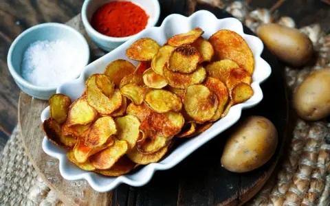 Selbstgemachte Kartoffelchips, goldbraun und knusprig, mit Salz und Paprikapulver daneben. So einfach kannst du Chips selber machen!