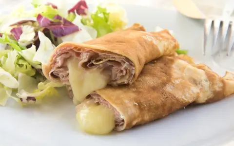 Zwei herzhafte Pfannkuchen mit Schinken und geschmolzenem Käse, serviert mit einem frischen Salat.