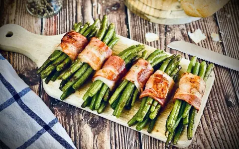 Grüne Bohnen, umwickelt mit knusprigem Speck, ein köstliches Speckbohnen Rezept, serviert auf einem Holzbrett.