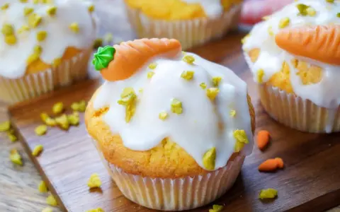 Leckere Karotten Muffins mit weißer Glasur und Marzipan-Karotten, bestreut mit gehackten Pistazien.
