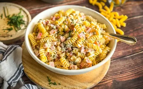 Ein cremiger, sommerlicher Nudelsalat mit Spiralnudeln, Schinkenwürfeln und Erbsen, garniert mit frischen Kräutern. Perfekt für warme Tage!