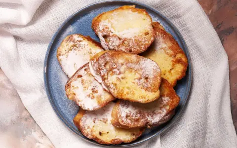 Armer Ritter, goldbraun gebacken und mit Puderzucker bestäubt, liegen auf einem blauen Teller.