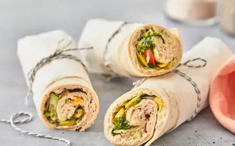 Drei leckere Thunfisch-Wraps, gefüllt mit Salat, Gurke und Tomate, sind in Papier gewickelt und mit Schnur verschnürt.