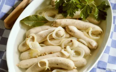 Saure Zipfel in einer Schüssel mit Zwiebelringen, Lorbeerblatt und Petersilie.