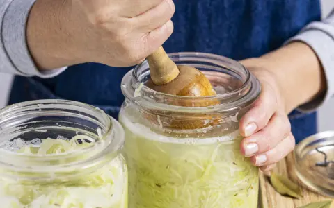 Hände pressen Kohl für ein einfaches Sauerkraut Rezept in ein Glas.