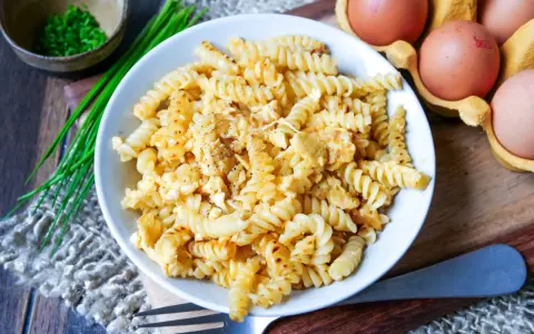 Fusilli-Nudeln mit Rührei, bestreut mit Pfeffer. Daneben liegen frische Eier und Schnittlauch. Ein einfaches Gericht: Nudeln mit Ei.