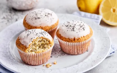 Drei köstliche zitronen mohn muffins mit Zuckerguss und Mohn bestreut, daneben frische Zitronen.