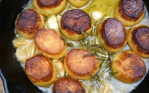 Goldbraun gebratene Fondant-Kartoffeln mit Rosmarin und Knoblauch in einer Pfanne.