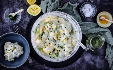 Cremiger Kartoffelsalat mit Joghurt, garniert mit Schnittlauch. Dazu Zitrone, Honig und grobes Salz.