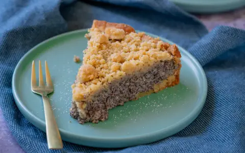 Ein saftiges Stück Mohnkuchen mit Streuseln auf einem mintgrünen Teller, daneben eine goldene Gabel. Ein köstliches Mohnkuchen Rezept.