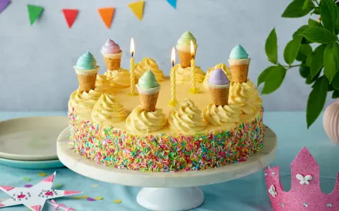 Bunte Torte mit Streuseln und Eiswaffel-Deko, perfekt für kinder torten rezepte einfach. Kerzen brennen, eine märchenhafte Feier beginnt.