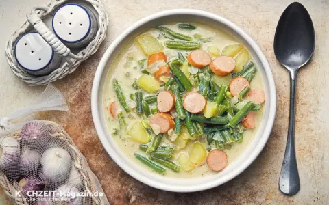 Herzhafte Bohnen-Kartoffel-Suppe mit Würstchen, ein Klassiker unter den Bohnen Rezepten. Dazu Salz- und Pfefferstreuer und frischer Knoblauch.
