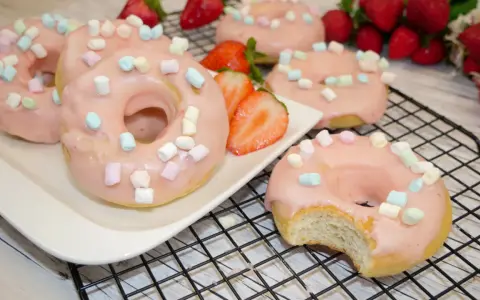 Leckere Donuts mit rosa Glasur und Marshmallows, perfekt für ein schnelles Donuts Rezept aus dem Backofen. Frische Erdbeeren garnieren das süße Gebäck.