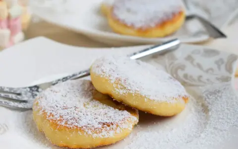 Zwei goldbraune Quarkkeulchen, bestäubt mit Puderzucker, liegen auf einem Teller. Ein einfaches Quarkkeulchen Rezept für süße Momente.