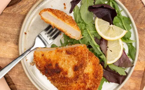 Knuspriges Kohlrabi-Schnitzel mit Salat und Zitrone auf einem Teller.