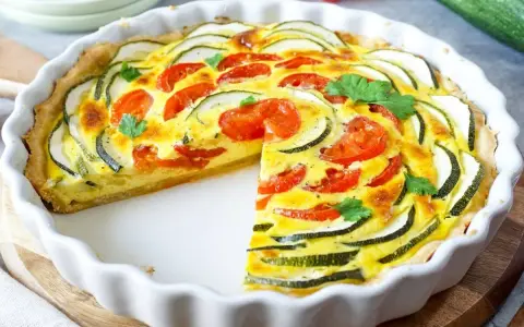 Eine köstliche Zucchini-Quiche mit Tomaten und frischer Petersilie, in einer weißen Quicheform, ein Stück fehlt.