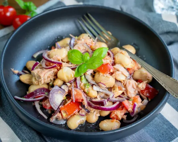 Herzhafter Thunfischsalat mit weißen Bohnen, Tomaten und roten Zwiebeln, garniert mit Basilikum. Ein köstlicher und einfacher Salat.