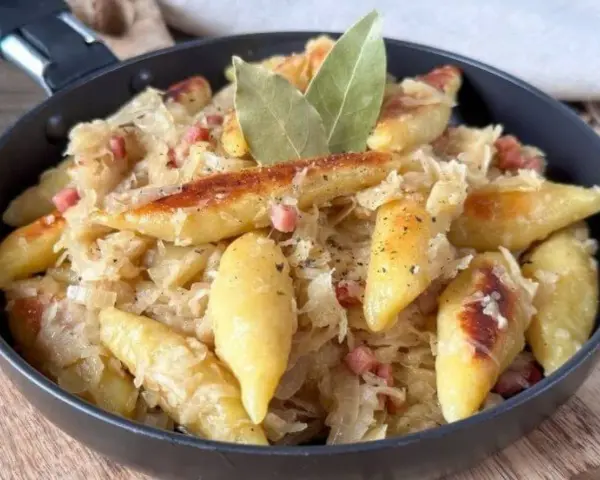 Schupfnudeln mit Sauerkraut, Speck und Lorbeerblättern in einer Pfanne. Ein herzhaftes Gericht, das zum Genießen einlädt.