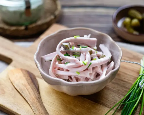 Schmackhaftes Fleischsalat-Rezept mit Gurkenstückchen und Schnittlauch garniert, serviert in einer Schale auf einem Holzbrett.