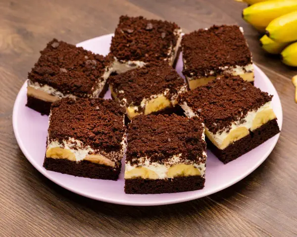 Saftiger Maulwurfkuchen vom Blech mit Bananen und Schokostreuseln auf einem rosa Teller.