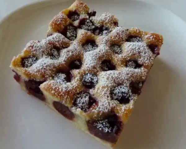 Zwei Stücke Kirschstreuselkuchen vom Blech, mit Puderzucker bestäubt, auf einem weißen Teller.