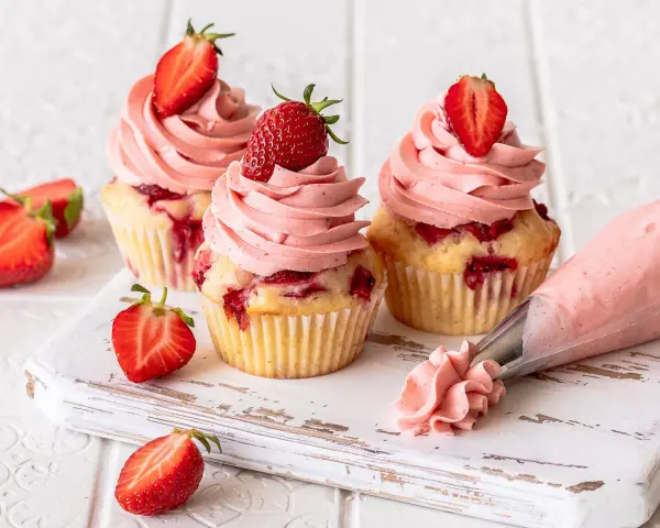 Erdbeer Cupcakes mit rosa Frosting und frischen Erdbeeren. Ein Spritzbeutel zeigt, wie die leckeren Erdbeer Cupcakes entstehen.